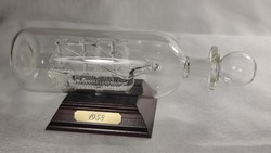 Fújt üvegbe fújt aprólékosan készült üveghajó. Rézlapra gravirozot 1958-as évszámmal. Fa talapzaton
