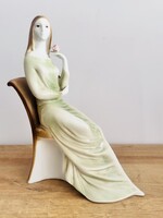 Zsolnay porcelán figura, amely egy széken ülő, zöld ruhás nőt ábrázol rózsával a kezében.