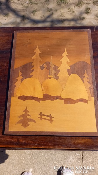 A picture of a wooden sheet depicting a pine landscape with a snowy cottage can be placed on a wall