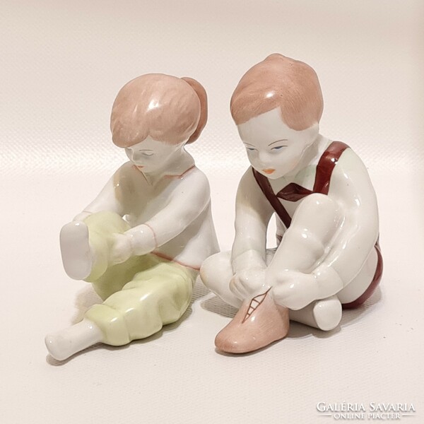 Little boy tying Aquincumi shoes and little girl getting dressed porcelain figures 2 pcs (2285)
