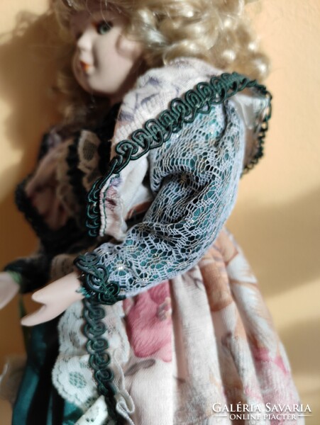 Porcelán fejű baba, szőke loknis kishölgy csipkés fodros virágos zöld ruhában