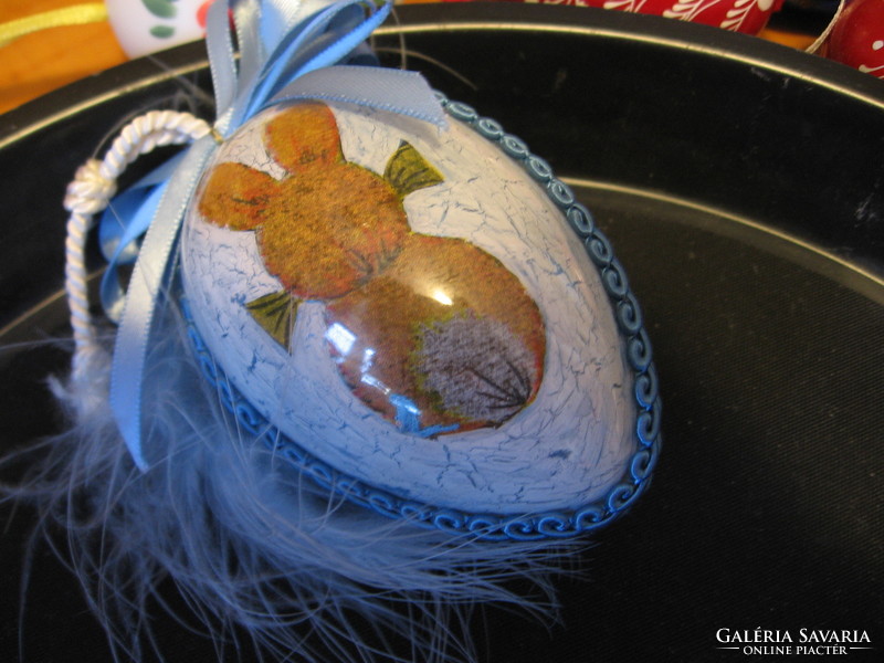 A painted plastic egg with feathers and a bunny inside