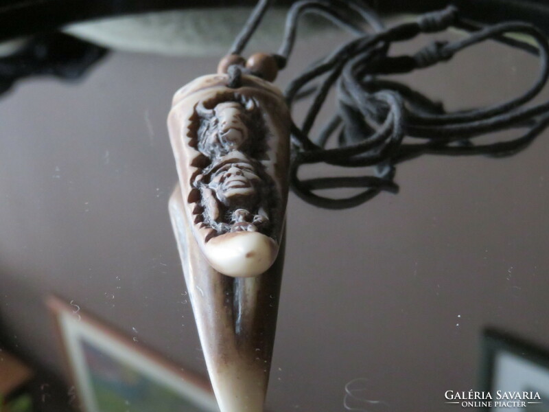 A carved bone of a tribal nature? Pendant on a strap decorated with wooden beads.