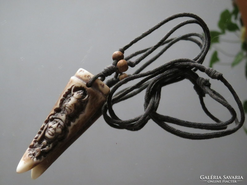 A carved bone of a tribal nature? Pendant on a strap decorated with wooden beads.