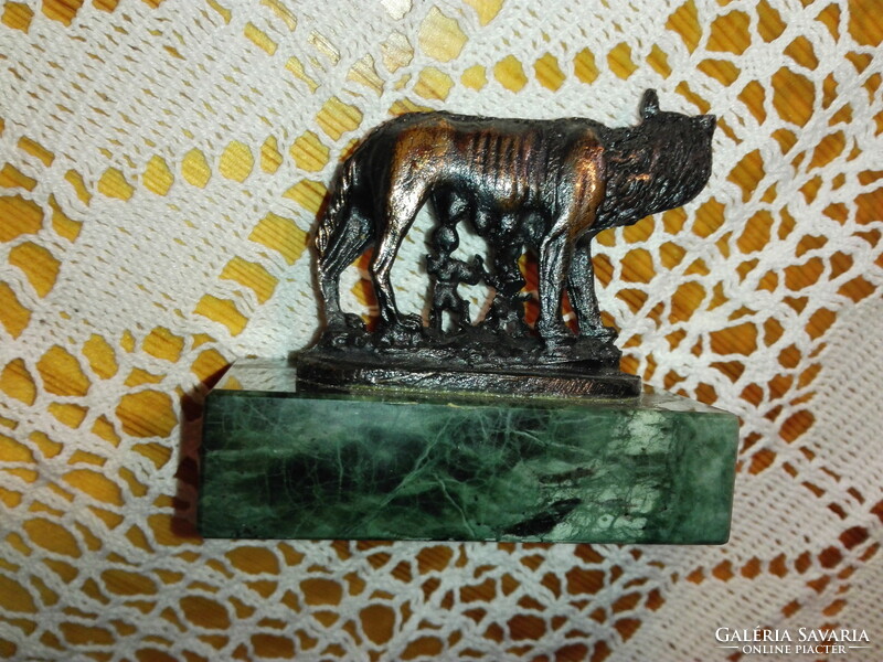 Red copper statue of Romulus and Remus on a marble plinth.
