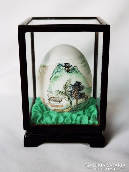 Old Chinese hand-painted egg in wooden holder behind glass