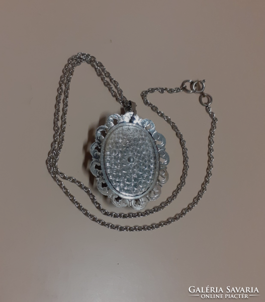 A silver-colored necklace with a pendant decorated with tapestry in a filigree silver-colored frame