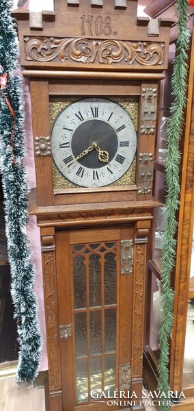 Faragott, tölgyfa hosszú tokos óra. Az óra tokja gótikus stílusú faragással és fém díszítőelemekkel